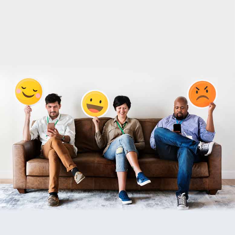 Three people on a couch holding emoji signs showing different moods