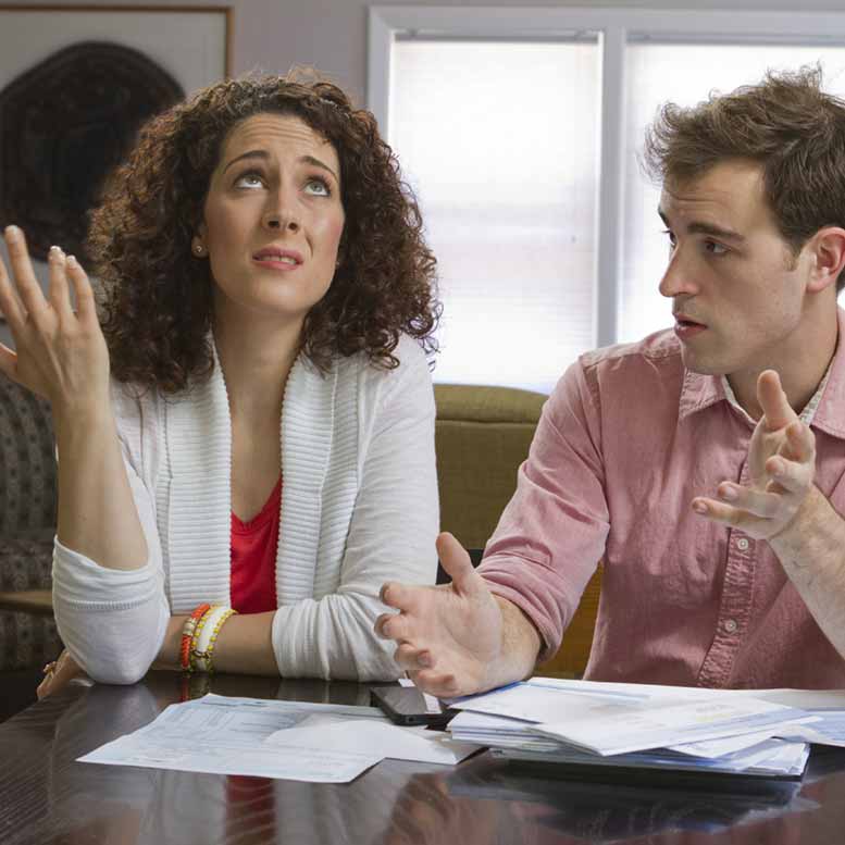 Couple stressed over finances, discussing bills at the table
