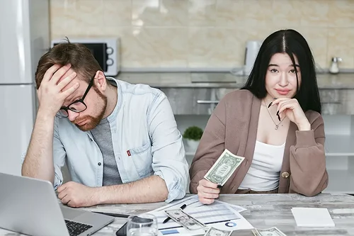 Stressed man reviewing finances while woman holds cash beside him