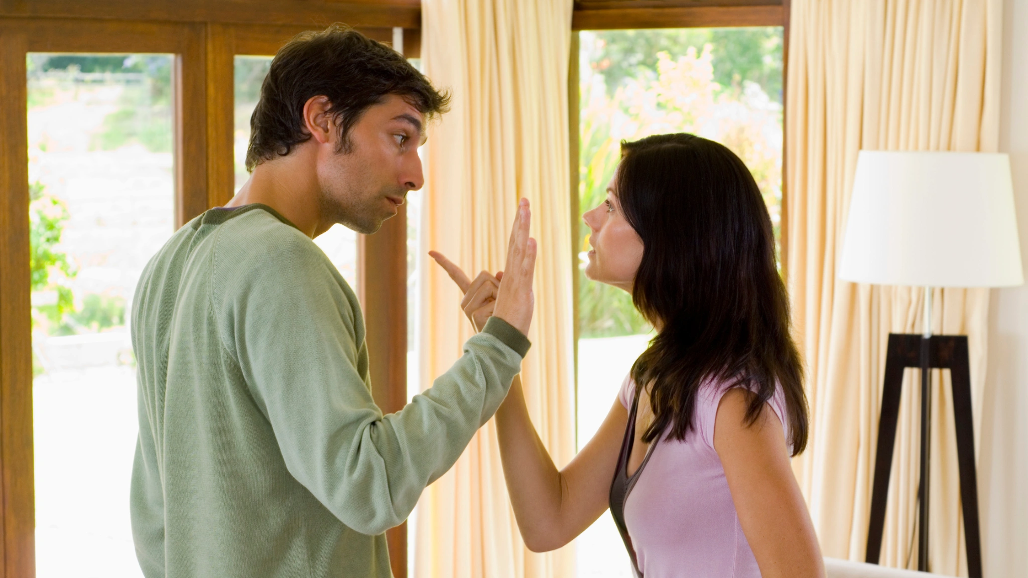 Couple arguing face to face in living room, representing relationship conflict