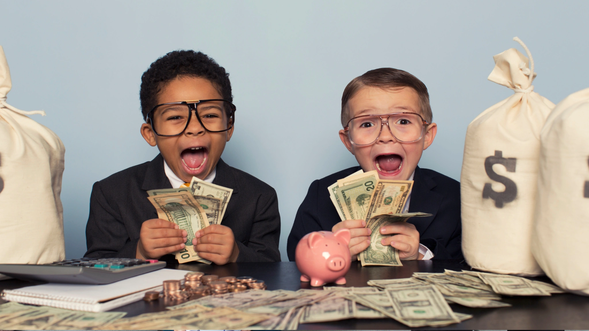 Two young boys in suits excitedly holding cash, illustrating early money habits and financial education